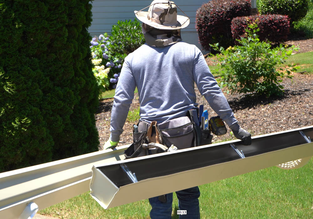 Back view of a Gutter Bro technician holding gutter sections with tools at the ready